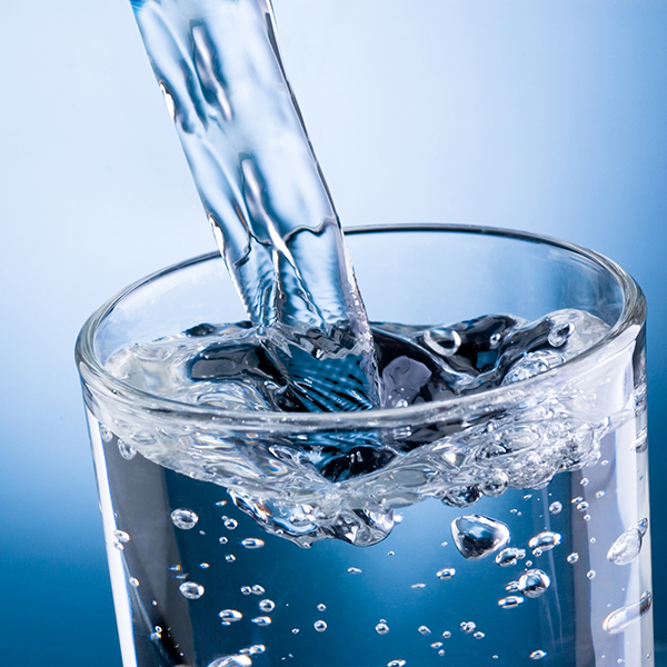 Pouring water into glass on blue background